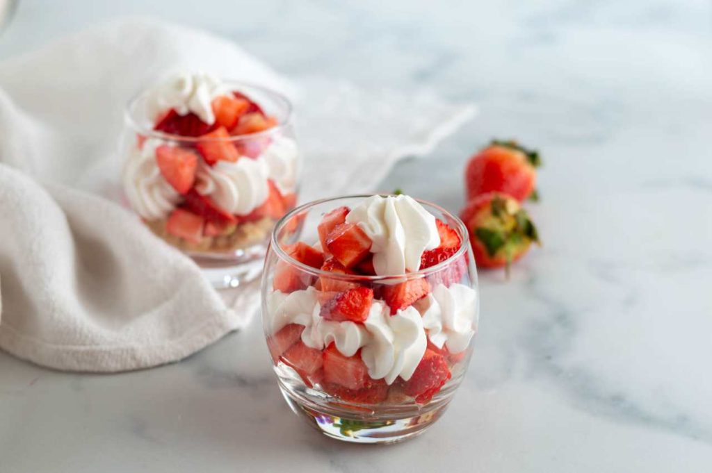 Dolce panna e fragole nel bicchiere, con strati di fragole fresche e panna montata, servito su fondo chiaro.