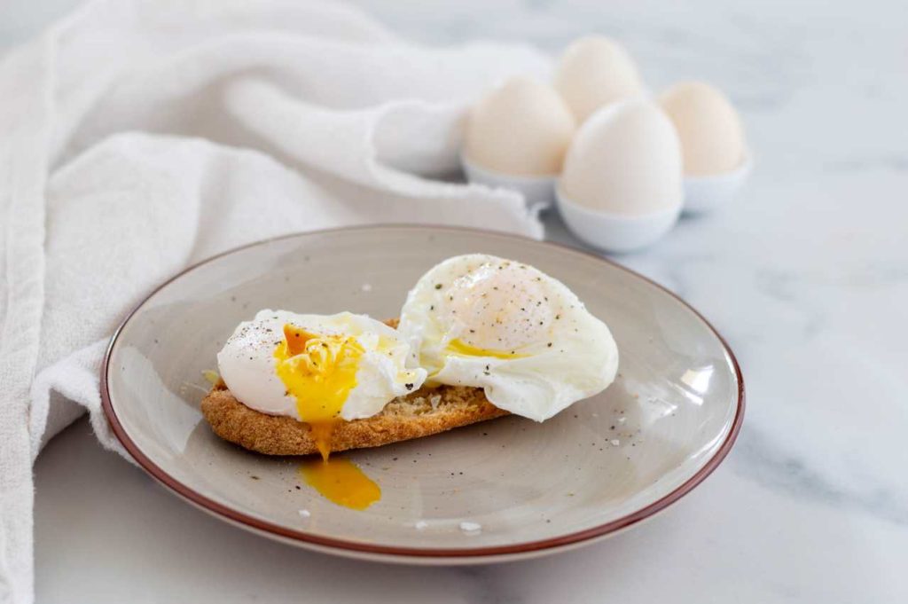 Uova in camicia con tuorlo morbido, servite su crostino e condite con pepe nero