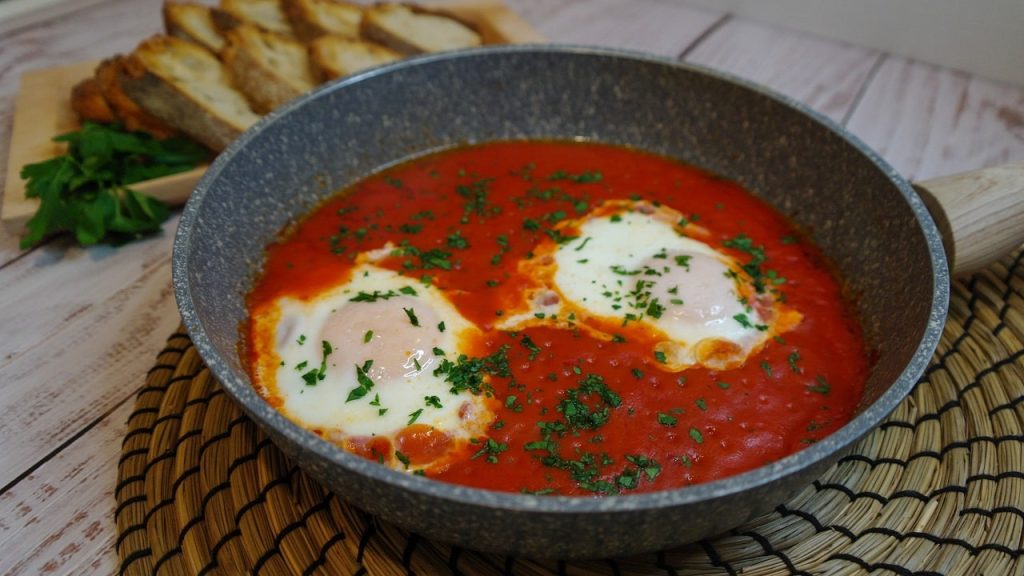 Uova in purgatorio cotte nel sugo di pomodoro, servite in padella con prezzemolo e pane tostato.