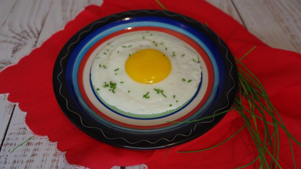 Uovo al tegamino con tuorlo morbido, guarnito con erba cipollina, servito su piatto colorato.