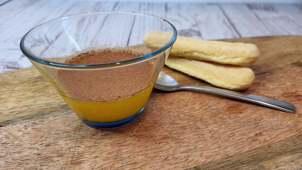 Uovo sbattuto con zucchero e cacao servito in ciotola di vetro, con biscotti sullo sfondo