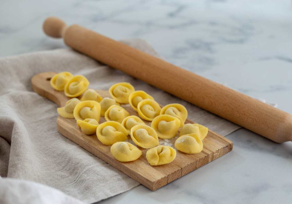 Cappelletti fatti in casa disposti su tagliere di legno con mattarello, pasta fresca della tradizione italiana