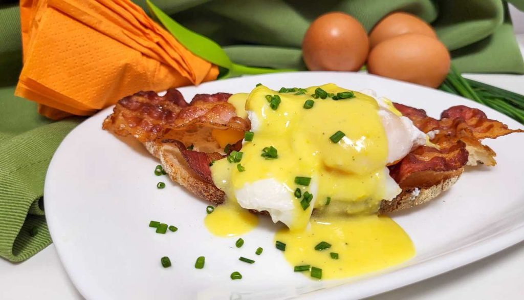 Uova alla Benedict con pancetta croccante e salsa olandese, servite su pane tostato, ricetta classica della colazione americana.