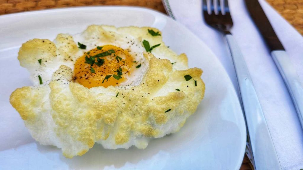 Uovo nuvola cotto al forno, con albume soffice e tuorlo morbido, servito su piatto bianco.