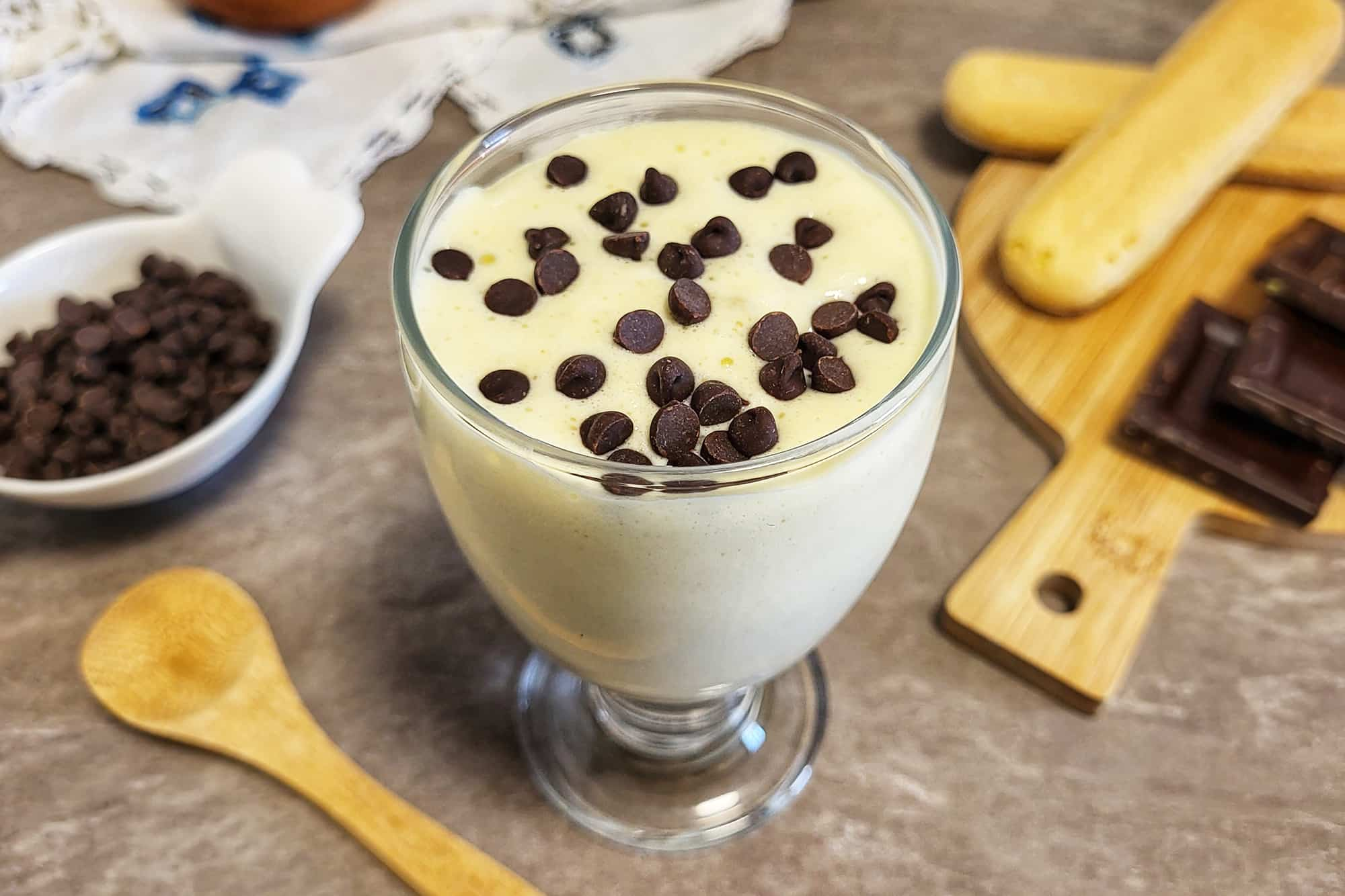 bicchiere con composto chiaro e gocce di cioccolato su un tavolo con cioccolato e accessori di legno