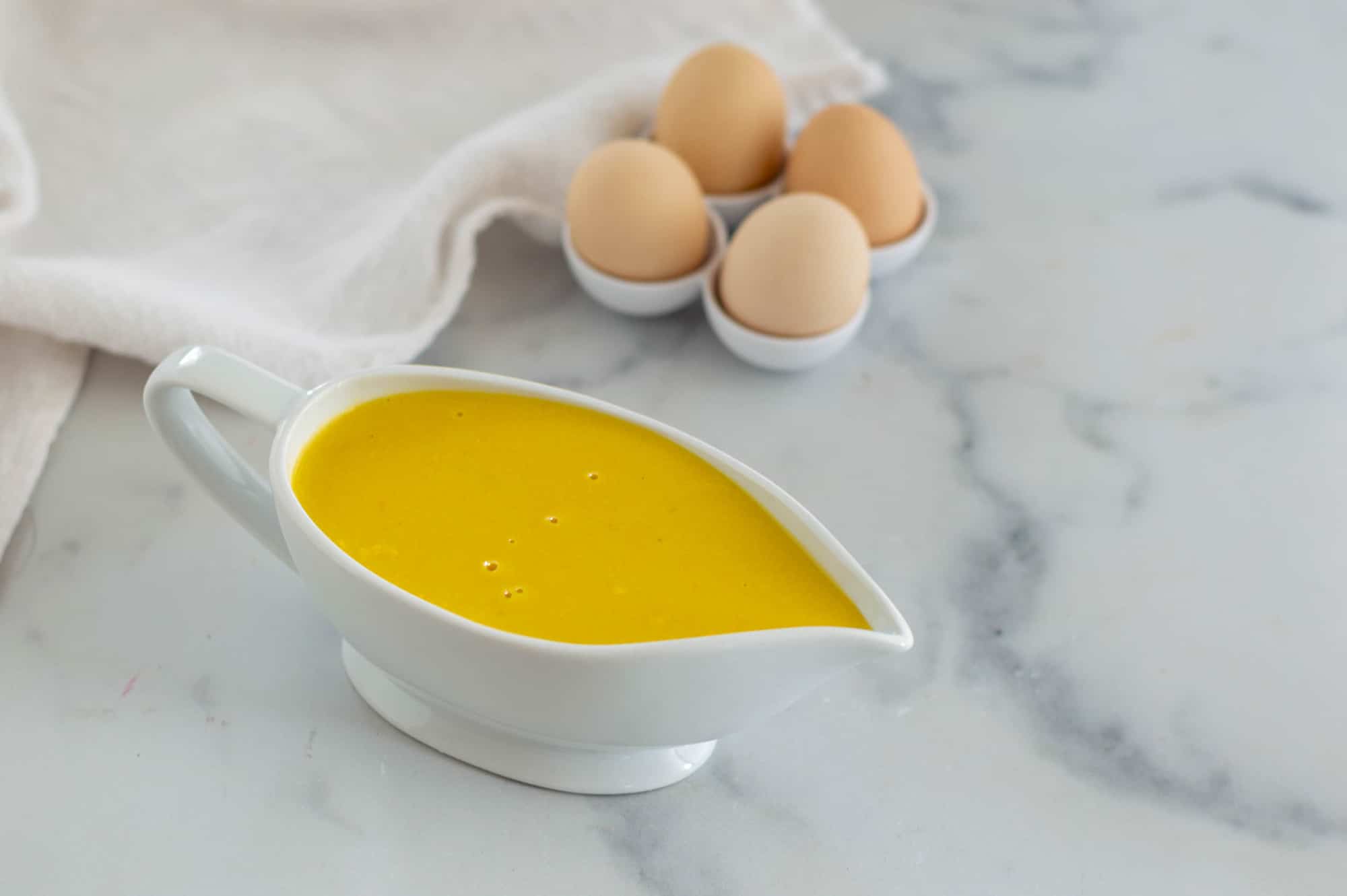 ciotolina con crema gialla, quattro uova e un canovaccio bianco su un tavolo di marmo
