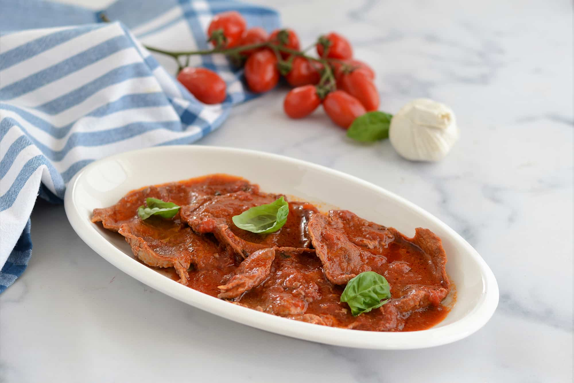 fettine di carne con pomodoro e basilico in piatto ovale bianco