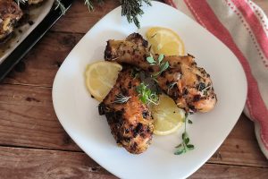 due cosce di pollo con tre fette di limone in un piatto bianco, su un tavolo di legno