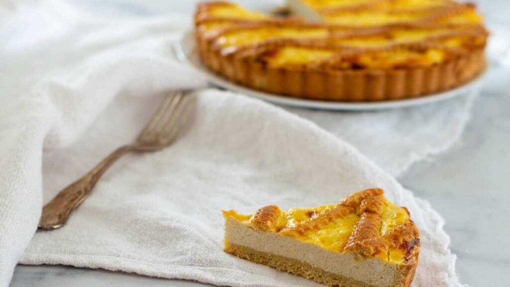Crostata di ricotta con base di pasta frolla e ripieno cremoso, cotta al forno e servita a fette su fondo chiaro.