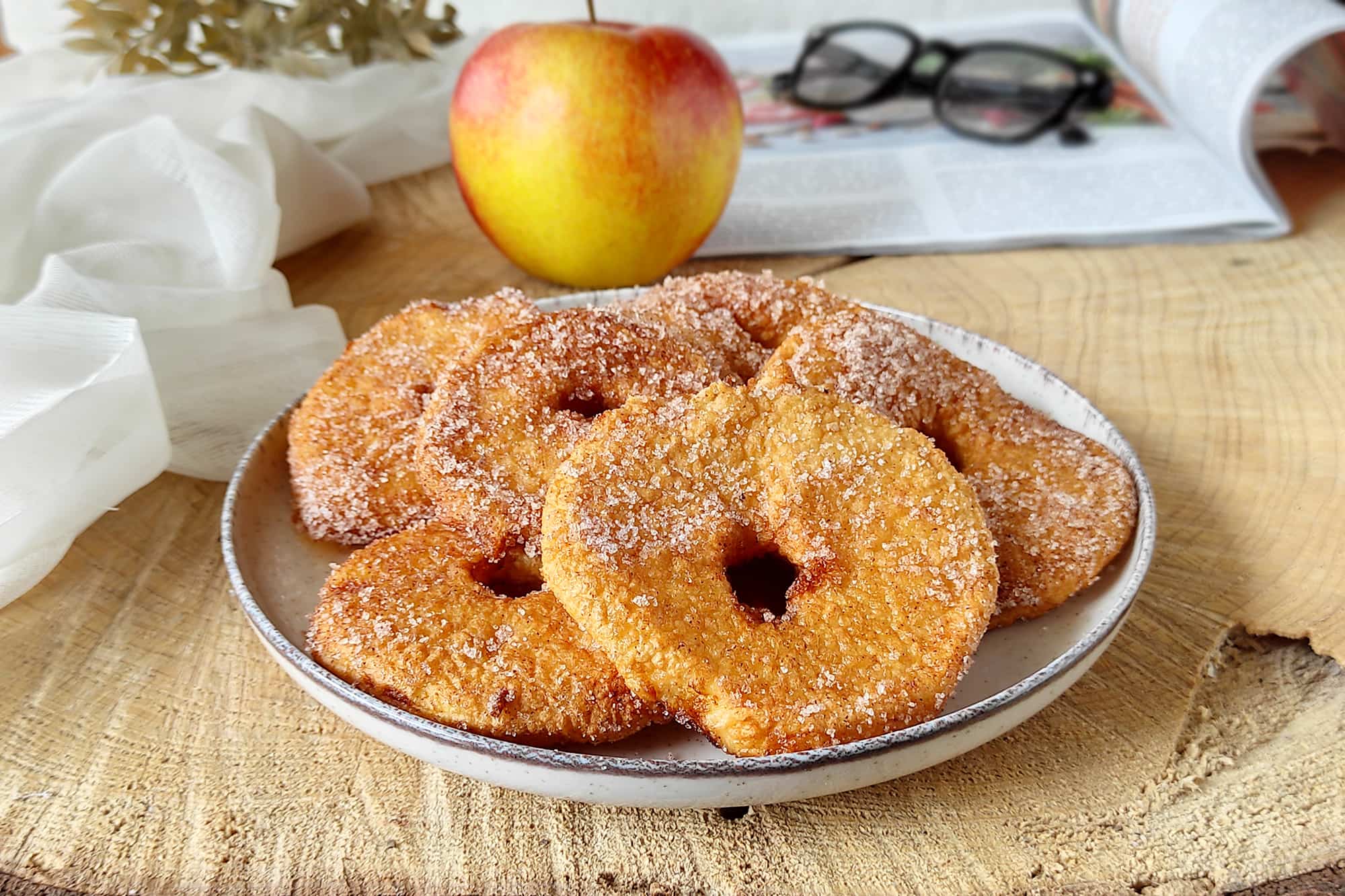 frittelle di mele ricoperte di zucchero su un piatto bianco, con una mela sullo sfondo