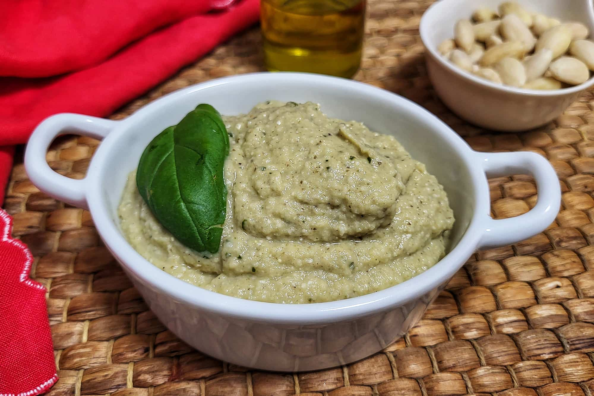 crema di melanzane dal colore verde con una foglia di basilico all'interno di un piatto bianco con i manici di ceramica