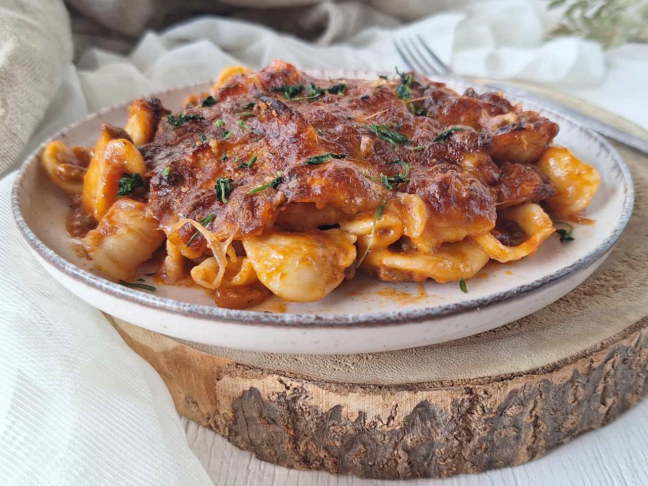 Piatto di pasta al forno con ragù e mozzarella filante servito su un piatto rustico.