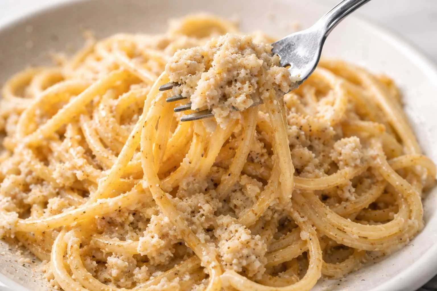 Spaghetti cacio e pepe cremosi con pecorino romano e pepe nero, serviti su piatto bianco