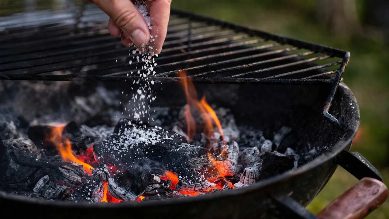 Sale grosso versato sulla brace accesa durante una grigliata, con carbone ardente e fiamme visibili